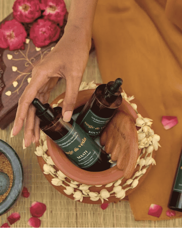 Woman reaching out for Maat Hair Oil bottle set against a luxury setting.